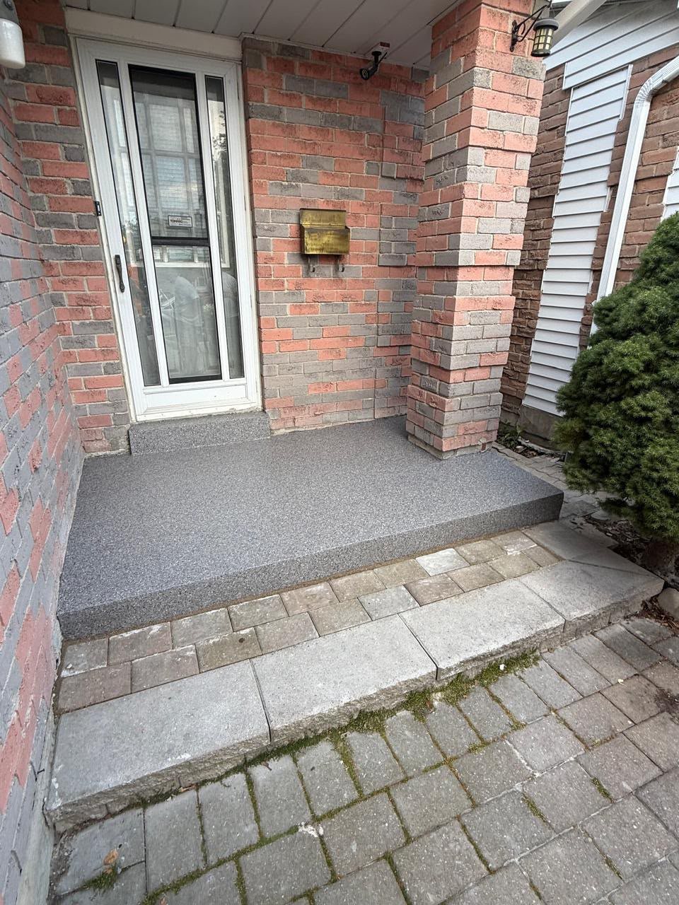 A Toronto front porch landing and step finished in a grey polyaspartic full-flake coating, meeting a brick wall and interlock walkway