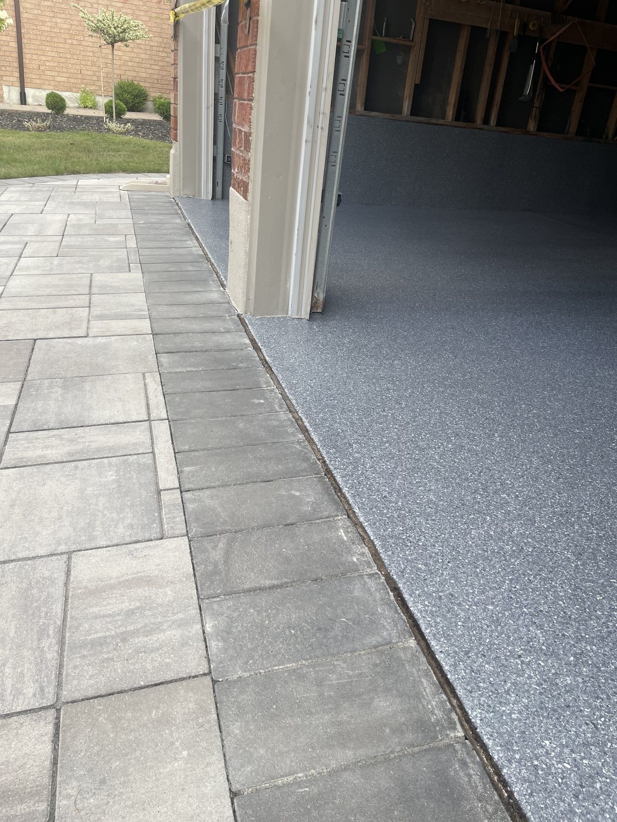 A garage floor in grey full-flake polyaspartic meeting the interlock driveway cleanly at the door line