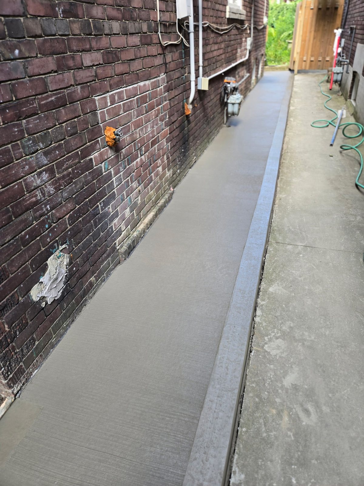 A newly poured concrete side walkway along a brick house, broom finish, freshly formed edge