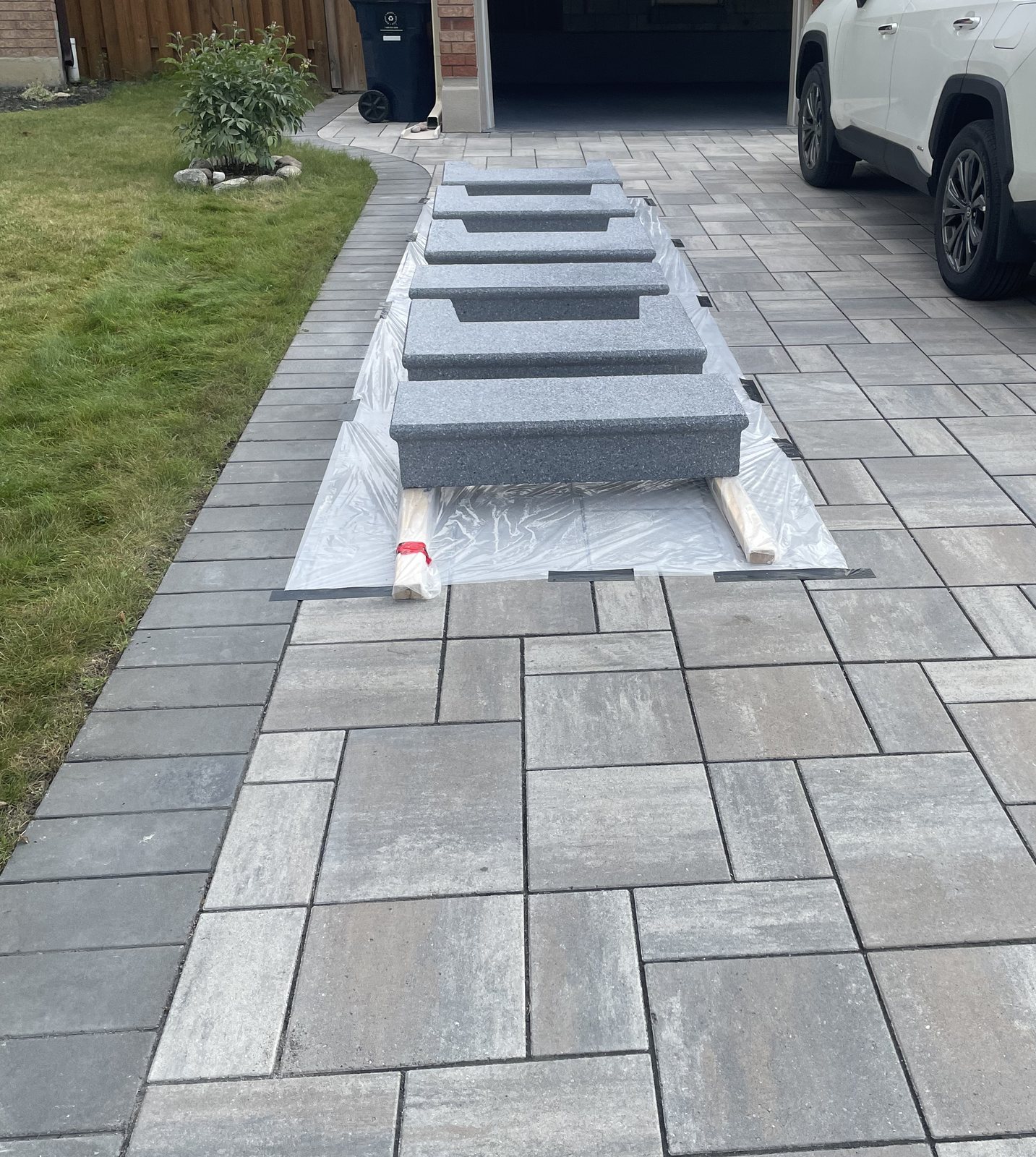 Precast concrete step units staged on protective sheeting across an interlock driveway before installation